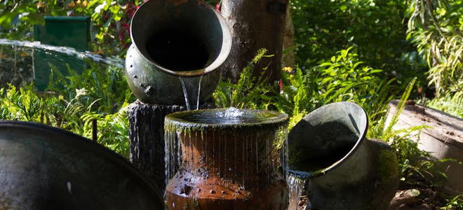 A grouping of ceramic and metal pots making up a fountain or pond in a yard. 