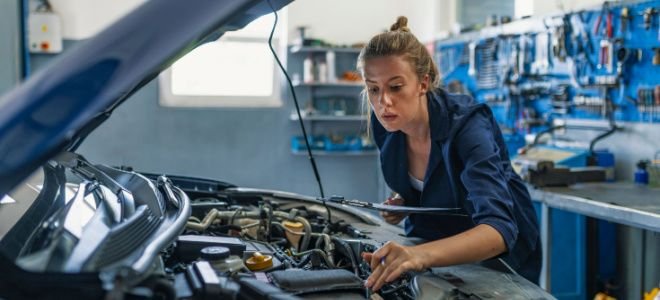 woman working under car hood in auto shop