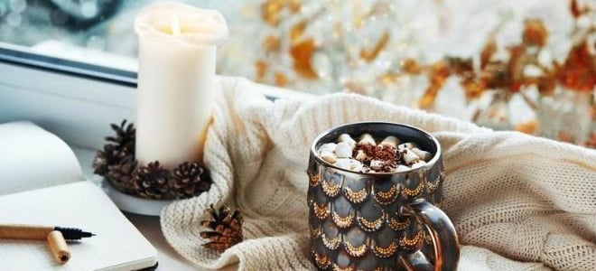 A pinecone-decorated candle with a cup of coffee and a book. 