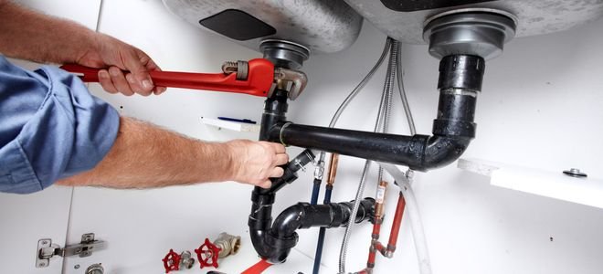 hands using wrench to adjust or install kitchen sink drain pipes