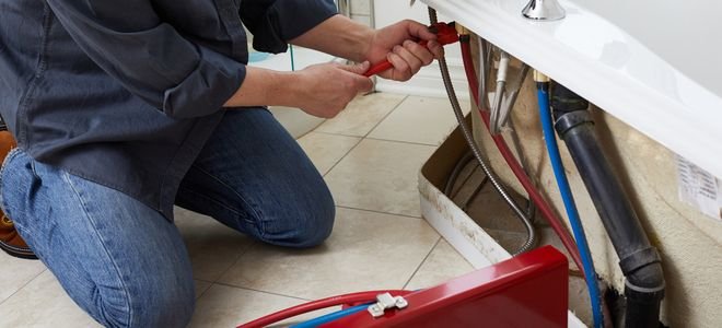 person fixing bathtub plumbing with wrench