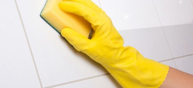 A yellow sponge cleaning a white tile wall. 