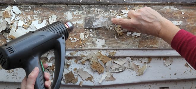 hands removing chipped paint with heat gun and scraper