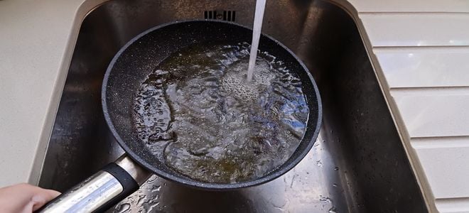 greasy pan in sink under running water