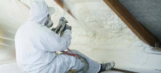 person in protective gear applying spray foam insulation under roof