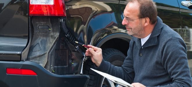 man inspects damage on a car with a clipboard