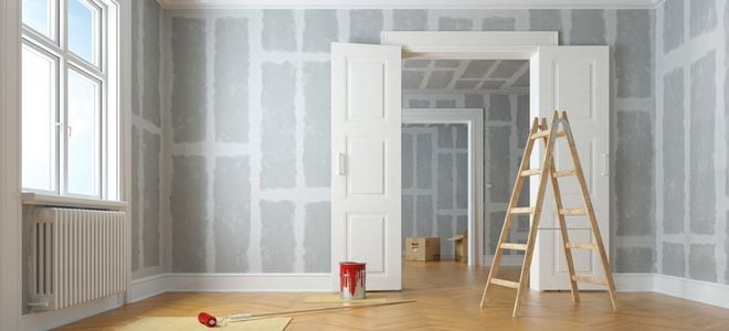 drywall surfaces on room undergoing remodeling or construction with large double doors and ladder near painting supplies
