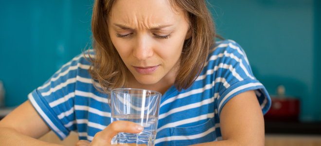 woman smelling a glass of water unhappily