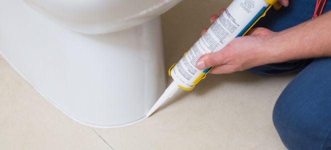 hands caulking the base of a toilet