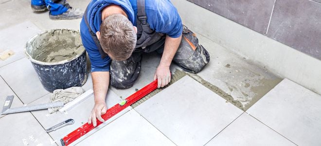 man laying large square tiles on bathroom floor