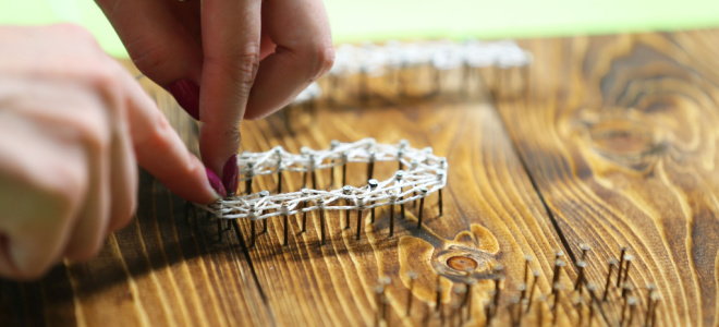 hands making string art with nails on a board