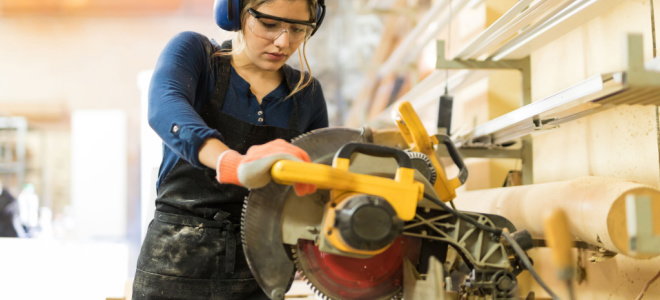 woman with safety goggles using power saw