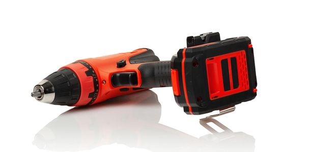 A red cordless drill on a reflective white surface