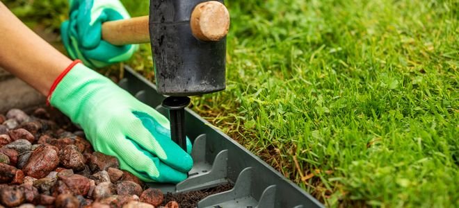 gloved hands with hammer installing plastic lawn edging