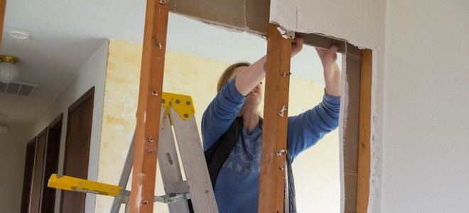 woman removing drywall from exposed studs