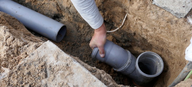 hand reaching into trench around drainage pipe