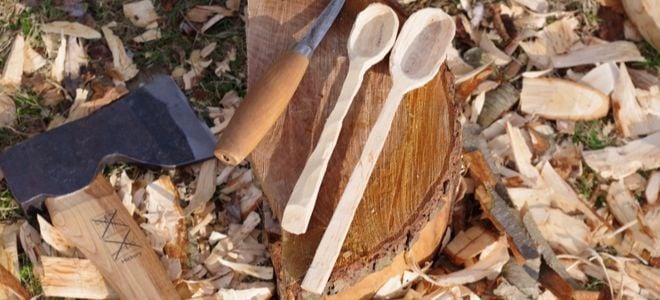whittled cooking spoons on a log with an axe