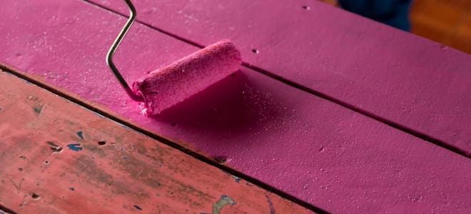 A paint roller applying bright pink on a wood table. 