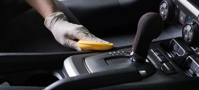 gloved hand cleaning interior car surface with sponge