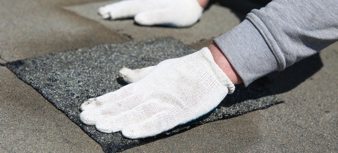 gloved hands applying roof shingle patch