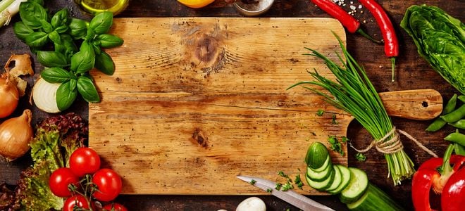 wooden cutting board surrounded by herbs and vegetables