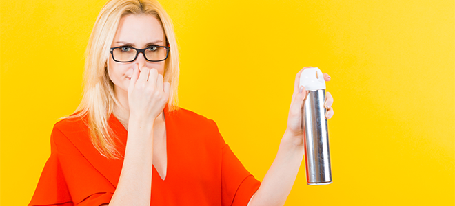 woman plugging nose and spraying air freshener