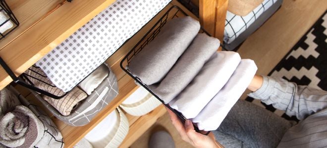hands putting folded clothes in an organized closet storage system
