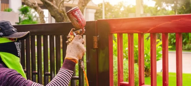 gloved hand spray painting metal fence