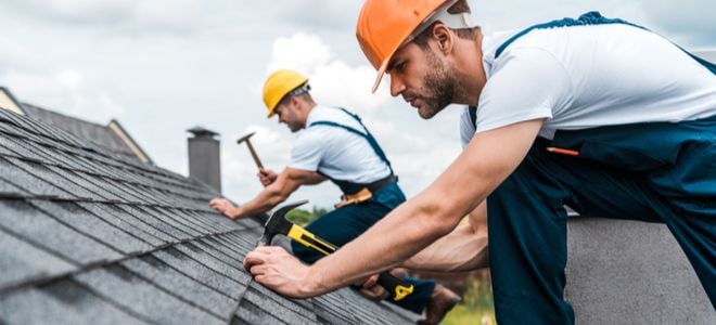 two workers nailing shingles onto roofing