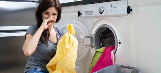 woman covering her nose near open washing machine with towels