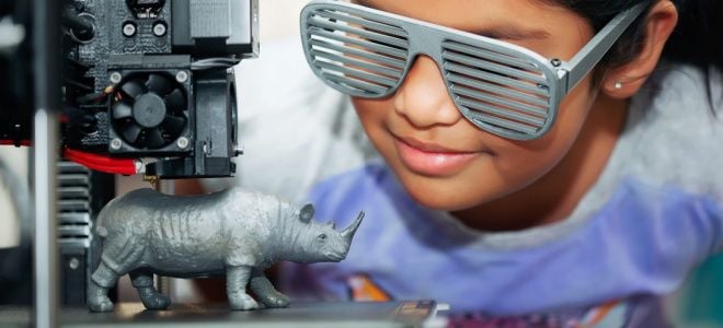 girl with sunglasses smiling at 3D printer making rhinoceros toy