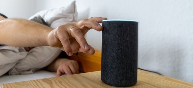 man touching smart speaker from bed