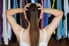 A girl holds her head while looking at a closet stuffed with hanging clothes