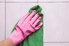 A pink gloved hand holding a green cloth against a shower wall. 