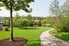A landscaped space with grass, trees, and a paved path. 