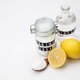 A jar of baking soda and vinegar against a white background with a couple of lemons. 