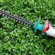 A gardener using an electric hedge trimmer to shape some thick hedges.