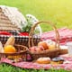 picnic basket and blanket laid out with fruit, donuts, mugs, and bread