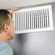 A man checking an air vent on a wall. 