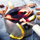 A metal pot with fruit slices and cinnamon sticks in and around it. 