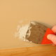 A closeup of a putty knife spreading spackle on a wall.