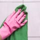 A pink gloved hand holding a green cloth against a shower wall. 