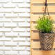 A hanging basket planter against a wood pallet and a white painted brick wall. 