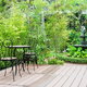 A garden fountain sits beside a backyard deck, surrounded by foliage.