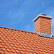 A red tiled roof with a brick chimney, topped with a chimney cap.