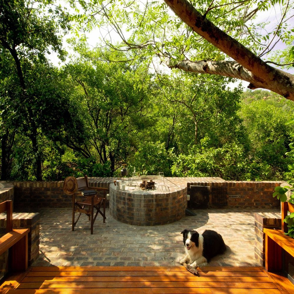 A dog rests happily by a stone fire pit on the House of the Big Arch's spacious outdoor terrace. 