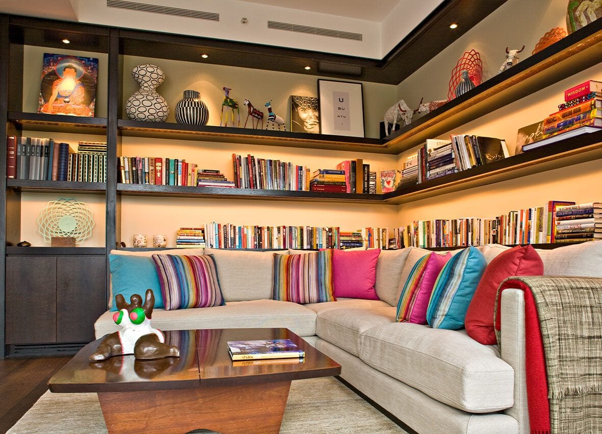 Colorful living area inside the lavish Jeffrey Beers-renovated apartment at 15 Central Park West, with lots of art and books visible on the shelves in the background.