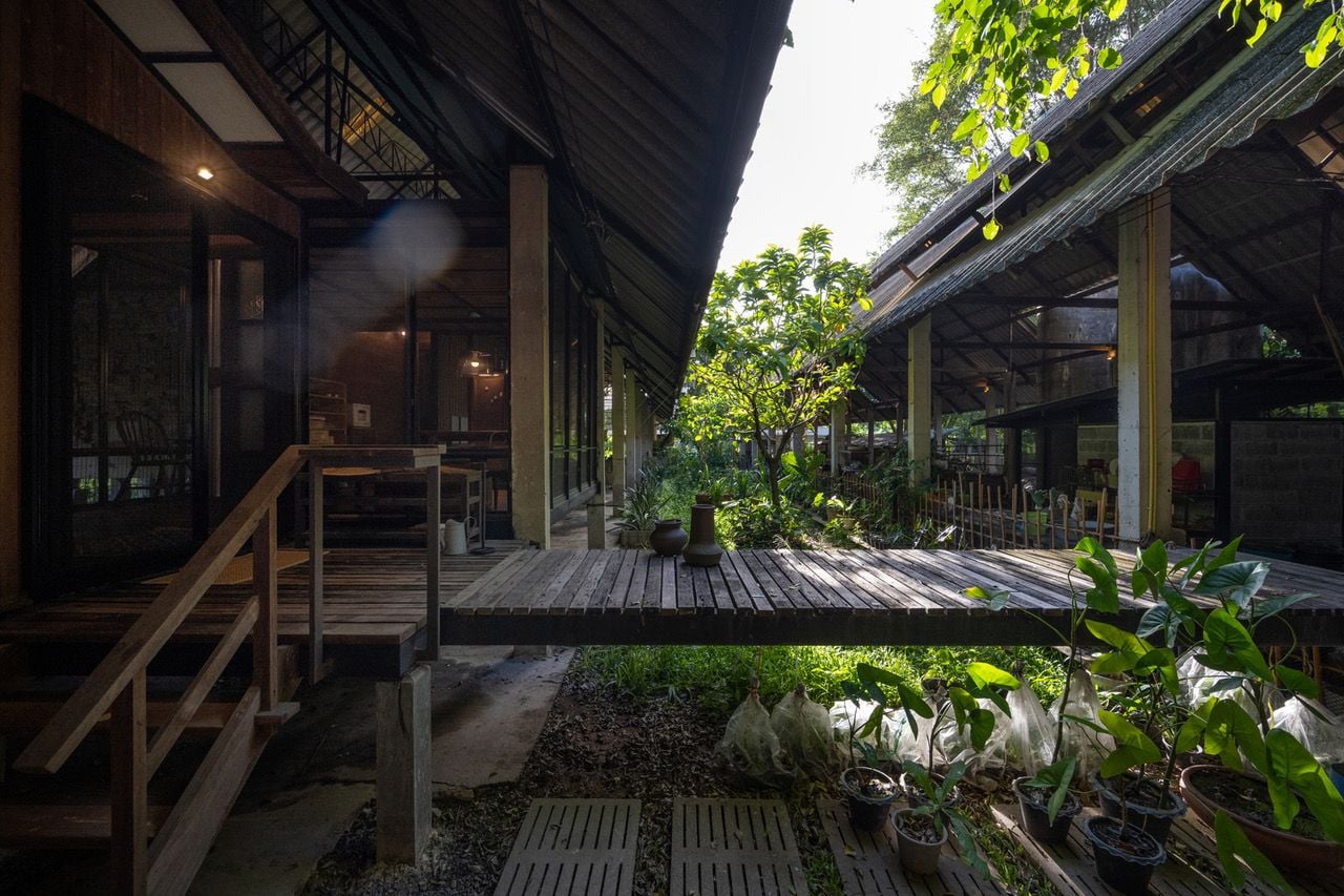 Reclaimed wooden walkway in the Kha-Nam Noi house runs between a plant nursery and a workshop. 