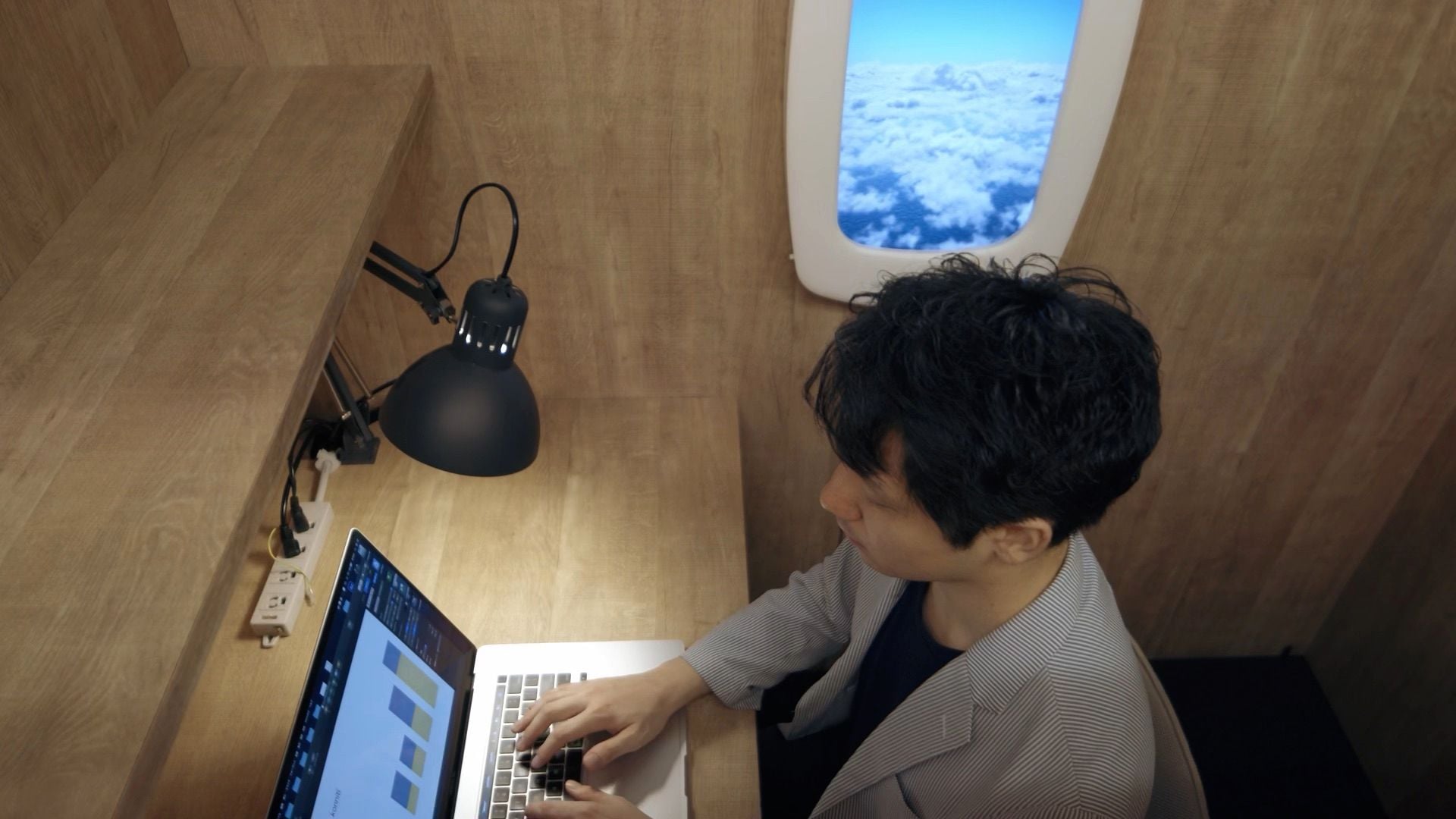 Man works at his desk while the Sky Scape digital airplane window displays a stunning view right next to him.