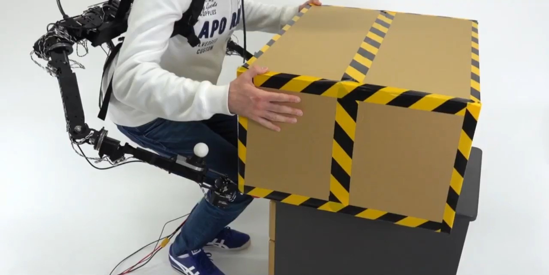 Man uses the ISL robo-arms' Power Assist mode to pick up a heavy box. 